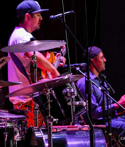 Baterista junto a sus platillos bajo luces violetas.