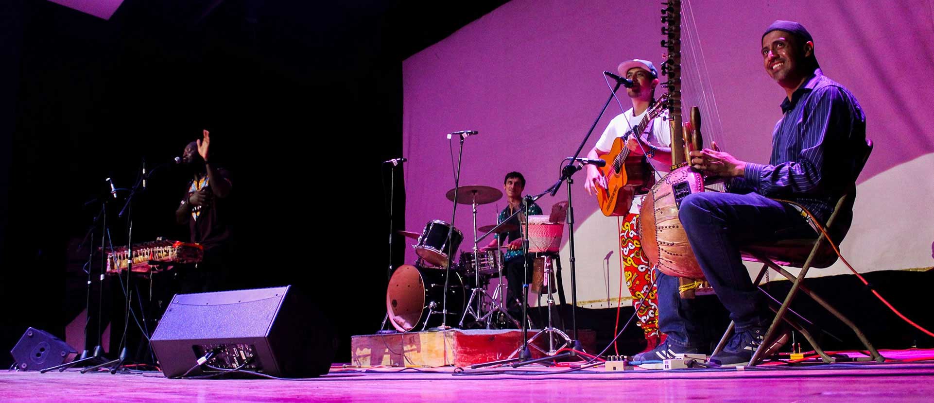 Músicos y percusionistas en un escenario iluminado en violeta.