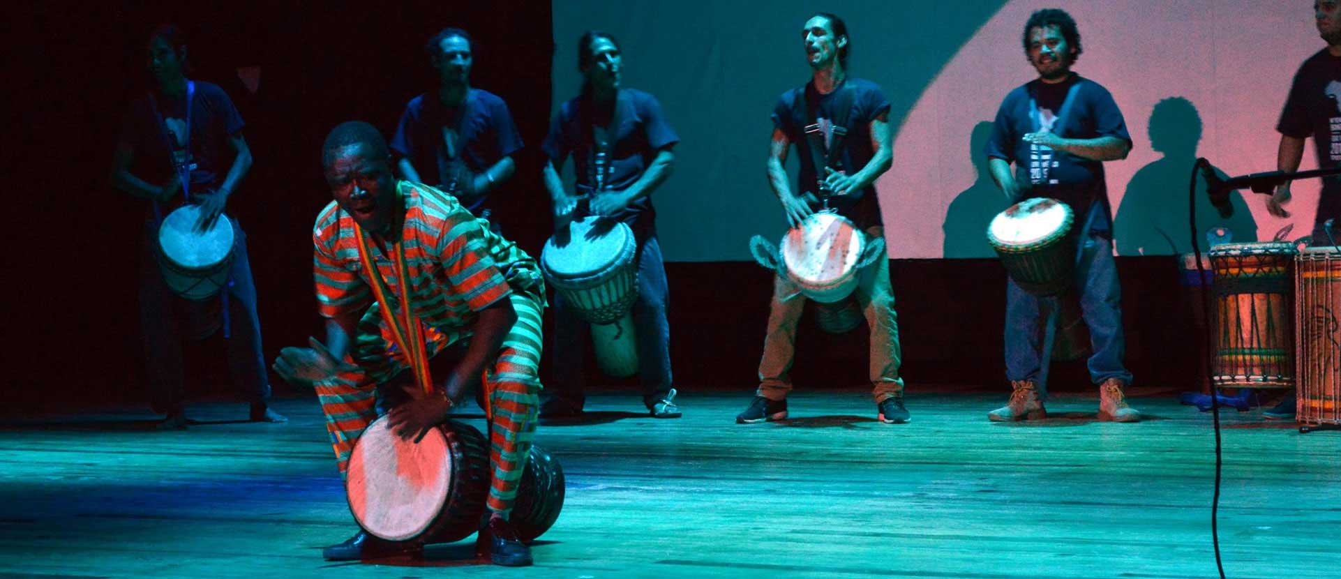 Un percusionista toca el djembé frente a un ensamble bajo luces azules.